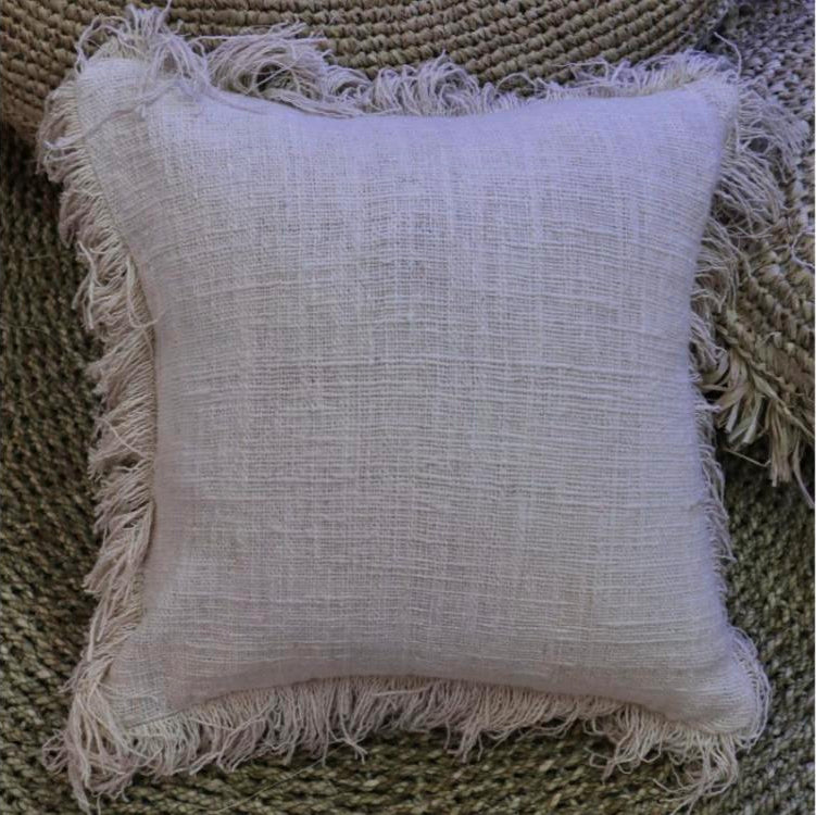 Fringed cotton cushion cover styled on a woven jute rug, showing its frayed edge detail